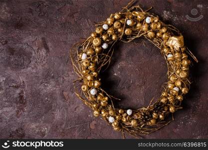 Golden woven natural wreath with acorns and pine cones on the brown marble wall. Golden woven wreath