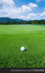 Golf ball above flag and green on tropical course in morning. Golf ball on tropical course