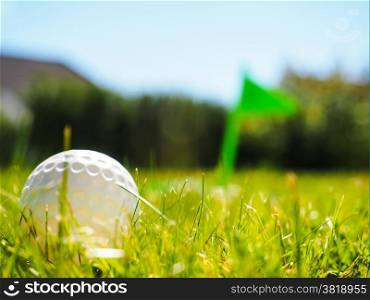 Golf ball laying in rough green grass approaching the tee with green flag