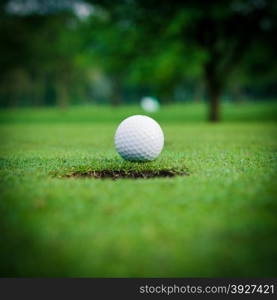 golf ball on lip of cup. Golf ball and hole