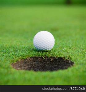 golf ball on lip of cup. Golf ball and hole