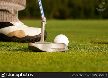Golf player attempting to put the ball in the hole, closeup on golf club, hole and feet of man