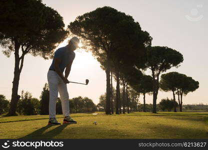 golf player hitting shot with club on course at beautiful morning with sun flare in background