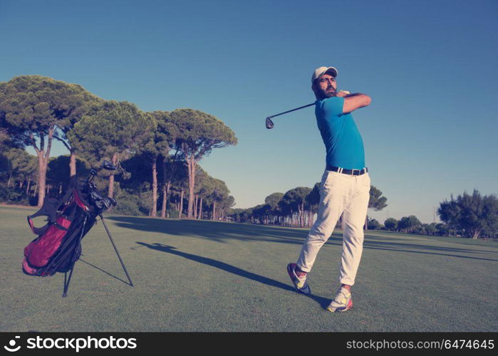 golf player hitting shot with club on course at beautiful morning with sun flare in background. golf player hitting shot
