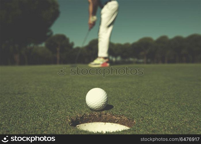 golf player hitting shot with driver, ball on edge of hole on course in background at beautiful sunny day. golf player hitting shot, ball on edge of hole