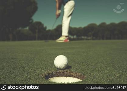 golf player hitting shot with driver, ball on edge of hole on course in background at beautiful sunny day. golf player hitting shot, ball on edge of hole