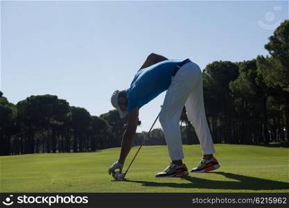 golf player placing ball on tee. beautiful sunrise on golf course landscape in background