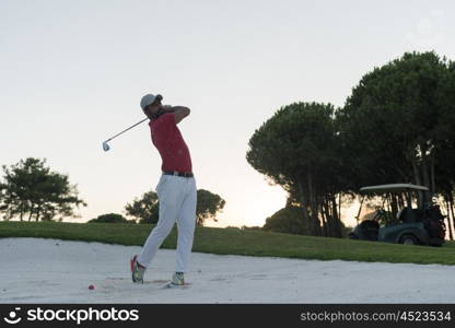 golf player shot ball from sand bunker at course with beautiful sunset with sun flare