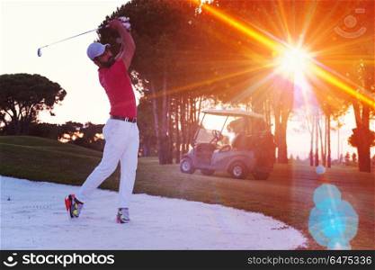 golf player shot ball from sand bunker at course with beautiful sunset with sun flare. golfer hitting a sand bunker shot on sunset