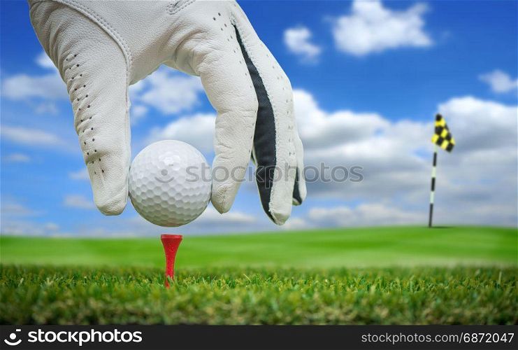 golf players hand placing ball on tee with blue sky