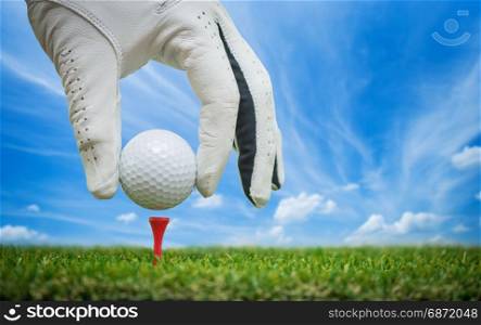 golf players hand placing ball on tee with blue sky