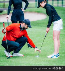 Golf putting lesson, two young female golfers practicing putting with golf instructor
