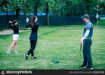 Golf swing technique ? golf instructor working with two young ladies on a golf range