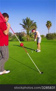 golf woman player putting golf ball and man holds flag