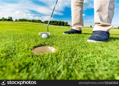 Golfer putting ball in the hole on a golf course close up. Focus on the ball.. Golfer putting ball in the hole on a golf course.