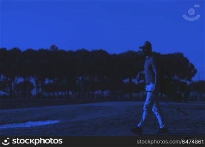 golfer walking and carrying golf bag at beautiful sunset. handsome middle eastern golfer carrying bag and walking to next hole at golf course on beautiful sunset in background duo tone