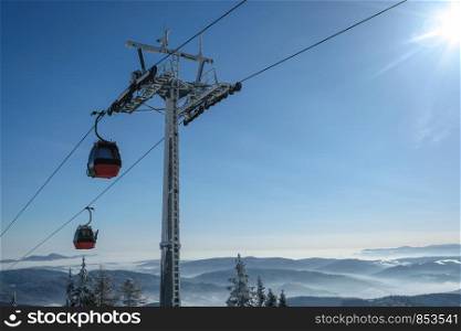 Gondola cabin lift in the ski resort over the forest on the background of snowy mountains in sunny day with copy space.