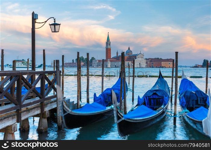 Gondolas moored by Saint Mark square with San Giorgio di Maggiore church in the background at twilight in Venice lagoon, Italia