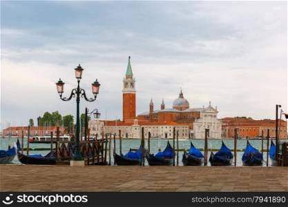 Gondolas moored by Saint Mark square with San Giorgio di Maggiore church in the background at twilight in Venice lagoon, Italia
