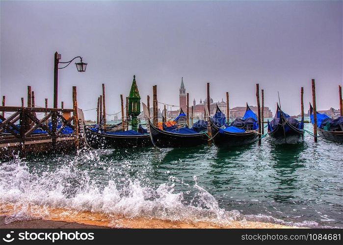 Gondolas parked at San Marco square with high tide and waves, Venice, Italy