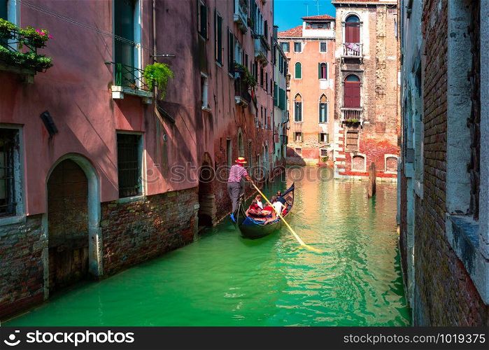 Gondolier carries tourists on Traditional gondola on a picturesque Venetian canal in sunny day, Venice, Italy.. Gondolas on Canal in Venice, Italy