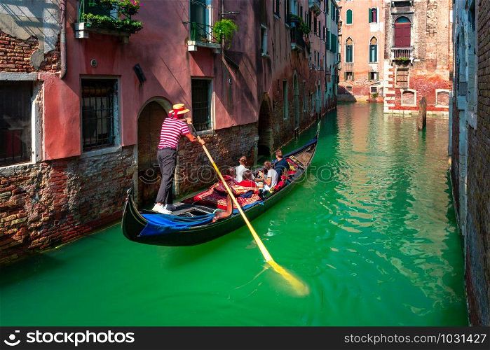 Gondolier carries tourists on Traditional gondola on a picturesque Venetian canal in sunny day, Venice, Italy.. Gondolas on Canal in Venice, Italy