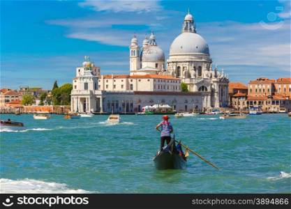 Gondolier in a gondola rides on Canal Grande in a hat with a red ribbon and a typical striped singlet, Basilica di Santa Maria della Salute in the background, Venice, Italy. Selective focus on Gondolier