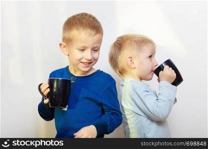 Good daily human hydration concept. Two boys, thirsty kids drinking drink from black mugs. Two boys kids drinking drink from mugs