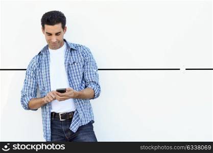 Good looking male wearing casual clothes writing with a smartphone. Young man texting on white urban background.
