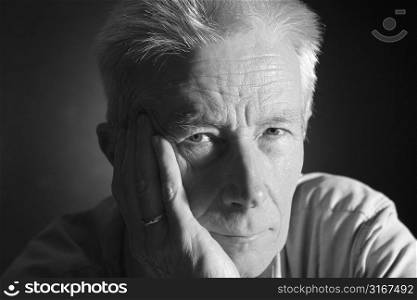 Good looking senior man leaning on his hand. Portrait taken in the studio over black
