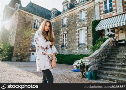 Good looking serious female model wears cape, poses against ancient castle, has excursion in old city, finds out historical facts, admires beauty of nature and landmarks. People, travelling concept