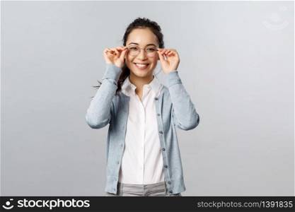 Good-looking young asian girl visit optician store, picking new pair of glasses, put-on eyewear and smiling satisfied, made-up her choice, standing pleased grey background.. Good-looking young asian girl visit optician store, picking new pair of glasses, put-on eyewear and smiling satisfied, made-up her choice, standing pleased grey background