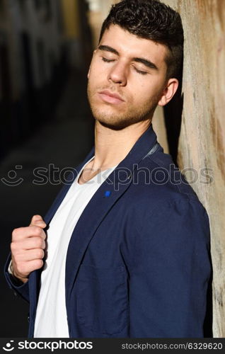 Good looking young man with blue eyes in the street. Model of fashion in urban background wearing white t-shir and blue jacket