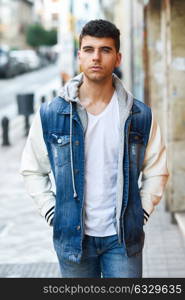 Good looking young man with blue eyes in the street. Model of fashion in urban background wearing white t-shirt, jeans and blue jacket