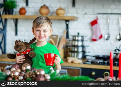 Good morning. A little boy drinks tea at the kitchen table and hugs a teddy moose. A time of miracles and fulfillment of desires. Merry Christmas.. Good morning. A little boy drinks tea at the kitchen table and hugs a teddy moose. A time of miracles and fulfillment of desires.