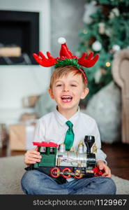 Good morning. Happy little boy with a gift, toy train, under the Christmas tree on a New Year&rsquo;s morning. A time of miracles and fulfillment of desires. Merry Christmas.. Good morning. Happy little boy with a gift, toy train, under the Christmas tree on New Year&rsquo;s morning. Time to fulfill wishes.