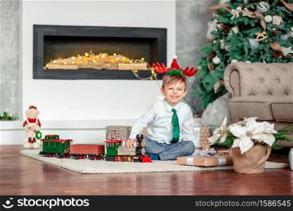Good morning. Happy little boy with a gift, toy train, under the Christmas tree on a New Year&rsquo;s morning. A time of miracles and fulfillment of desires. Merry Christmas.. Good morning. Happy little boy with a gift, toy train, under the Christmas tree on New Year&rsquo;s morning. Time to fulfill wishes.
