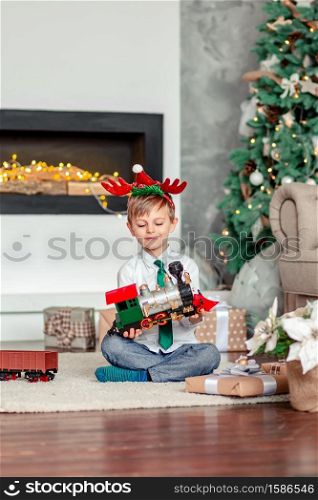 Good morning. Happy little boy with a gift, toy train, under the Christmas tree on a New Year&rsquo;s morning. A time of miracles and fulfillment of desires. Merry Christmas.. Good morning. Happy little boy with a gift, toy train, under the Christmas tree on New Year&rsquo;s morning. Time to fulfill wishes.