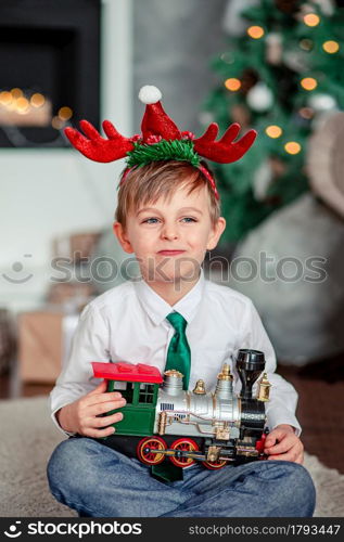 Good morning. Happy little boy with a gift, toy train, under the Christmas tree on a New Year&rsquo;s morning. A time of miracles and fulfillment of desires. Merry Christmas.. Good morning. Happy little boy with a gift, toy train, under the Christmas tree on New Year&rsquo;s morning. Time to fulfill wishes.