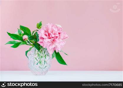 Good morning. Pink peonies in a crystal vase on a pink wood background, copy space, close up.. Pink peonies in a crystal vase on a pink wood background.