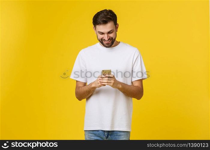 Good news from friend. Confident young handsome man in jeans shirt holding smart phone against yellow background.. Good news from friend. Confident young handsome man in jeans shirt holding smart phone against yellow background