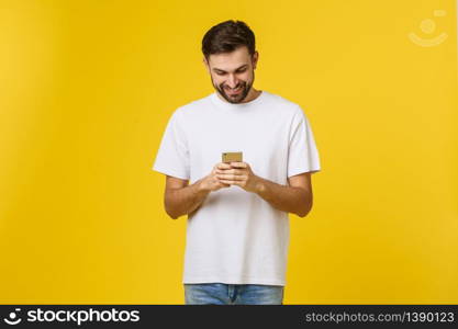 Good news from friend. Confident young handsome man in jeans shirt holding smart phone against yellow background.. Good news from friend. Confident young handsome man in jeans shirt holding smart phone against yellow background