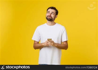 Good news from friend. Confident young handsome man in jeans shirt holding smart phone against yellow background.. Good news from friend. Confident young handsome man in jeans shirt holding smart phone against yellow background