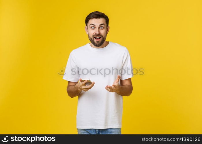 Good news from friend. Confident young handsome man in jeans shirt holding smart phone against yellow background.. Good news from friend. Confident young handsome man in jeans shirt holding smart phone against yellow background