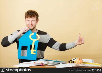Good purchase concept. Male buyer with paper model of house and key. Smiling positive man buying his first real estate flat building. . Man with house and key.