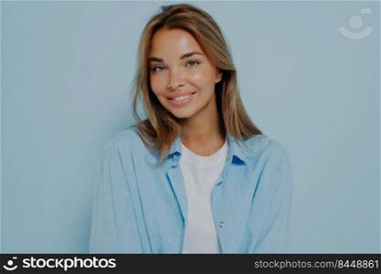 Gorgeous European women with beautiful hair and clean skin smiling at camera, being happy about her day and future date, posing on light blue background. Human face expression. Gorgeous woman with clean skin posing on light blue background