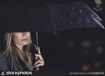 Gorgeous sad woman standing under big black umbrella on rainy night, half face, walking under downpour, loneliness and sadness concept. Loneliness and sadness concept