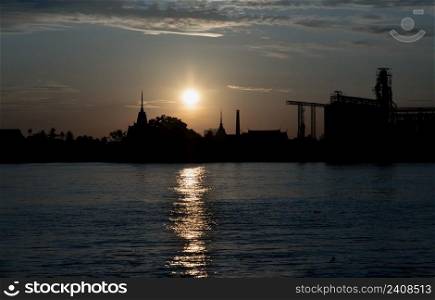Gorgeous scenic of Thai temple silhouettes and Industrial factory along Chao phraya river over sun at sunrise. Travel attraction in Thailand, Space for text, Focus and blur.