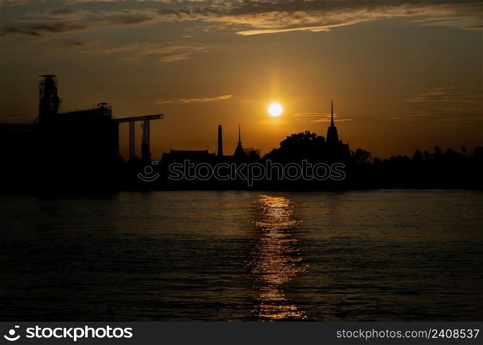 Gorgeous scenic of Thai temple silhouettes and Industrial factory along Chao phraya river over sun at sunrise. Travel attraction in Thailand, Space for text, Focus and blur.