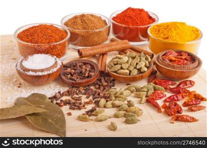 gorgeous setting with cooking spices and herbs (bay leaves, chili powder, cloves, cardamom pods, cinnamon sticks, garam masala, paprika, piri piri, salt, turmeric) on a wooden mat (isolated on white background)